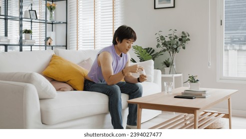 Young adult real gay LGBT man pouring bottle take pill drink water glass sit at home sofa couch. Gen Z asia people LGBTQ male or non binary gender happy smile eat beauty skin health care medical drug. - Powered by Shutterstock