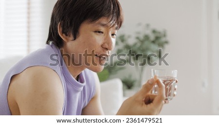 Young adult real gay LGBT man pouring bottle take pill drink water glass sit at home sofa couch. Gen Z asia people LGBTQ male or non binary gender happy smile eat beauty skin health care medical drug.