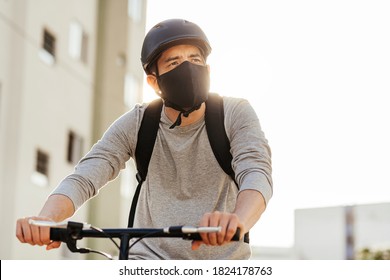 Young adult riding a bicycle through the city wearing face mask against COVID-19 - Powered by Shutterstock