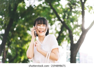 Young adult southeast asian business single woman using smartphone talking with friend. Happy face and laugh. City break lifestyle working people. Backgroud at outdside on day.
