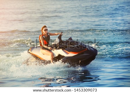 Young adult sporty caucasian woman riding jet ski in ocean blue water at warm evening sunset. Beach extreme sport activities and recreation