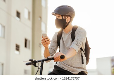 Young adult standing on bicycle using smartphone in the city wearing face mask against COVID-19 - Powered by Shutterstock