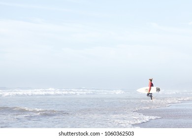 Young adult surfer with dreadlocks wearing wetsuit entering foggy ocean with surfboard under arm to catch waves during summer evening surf session - active lifestyle and surfing concept, copy space - Shutterstock ID 1060362503