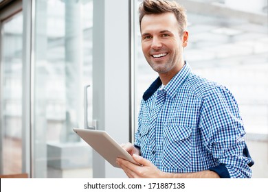 Young adult with a tablet in his hand and smiling into the camera
