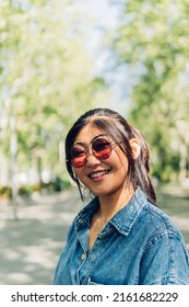 Young Adult Woman 20s, With Asian Features, Looking At Camera With Sunglasses In Summer. Japanese Student Smiling, Happy, Confident And Carefree.