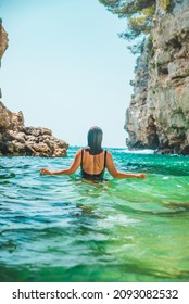 Young Adult Woman In Black Swimsuit Walking Into Sea Between Rocks Cliff Summer Beach Vacation