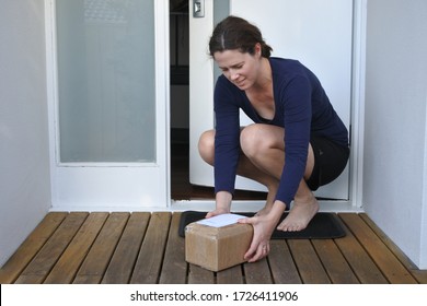 Young Adult Woman Collecting A Package Postal Box Courier Delivery From Home Doorstep Front Porch.