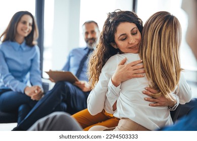 Young adult woman embracing and supporting friend during support group therapy session with diverse women. Two women hug in therapy session. Group therapy session, empathy concept - Powered by Shutterstock