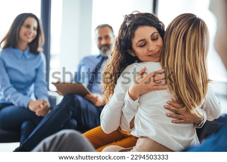 Young adult woman embracing and supporting friend during support group therapy session with diverse women. Two women hug in therapy session. Group therapy session, empathy concept