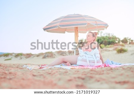 Young adult woman with a fit body wears a bikini with a thong while enjoying a day under a parasol at the beach during summer vacations on the Mediterranean coast of Guardamar.