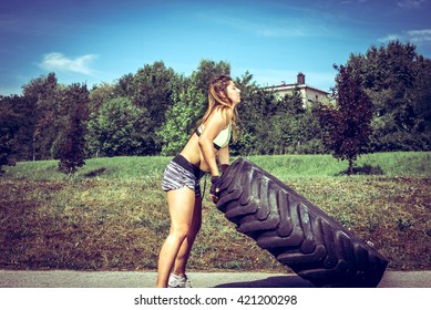 Young adult woman flipping and rolling tire during  exercise outdoor. Toned image. - Powered by Shutterstock