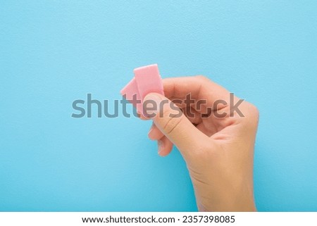 Young adult woman hand fingers holding and showing two pink sweet chewing gum pads on light blue table background. Pastel color. Closeup.