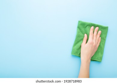 Young Adult Woman Hand Holding Green Rag And Wiping Table, Wall Or Floor Surface In Kitchen, Bathroom Or Other Room. Closeup. Empty Place For Text Or Logo. Light Blue Background. Pastel Color.