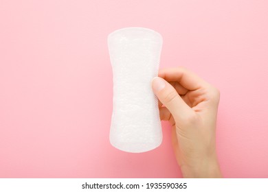 Young adult woman hand holding new white panty liner on light pink table background. Pastel color. Closeup. Female daily hygiene.