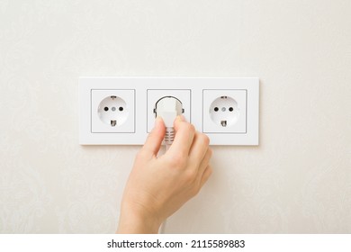 Young adult woman hand holding and plugging white electrical plug in wall outlet socket at home. Closeup. - Shutterstock ID 2115589883