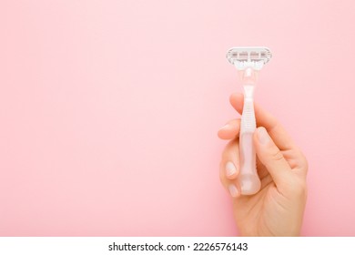 Young adult woman hand holding razor on light pink table background. Pastel color. Closeup. Female product for smooth body skin. Empty place for text.