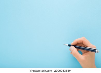 Young adult woman hand holding pen and writing on light blue background. Pastel color. Closeup. Empty place for text.