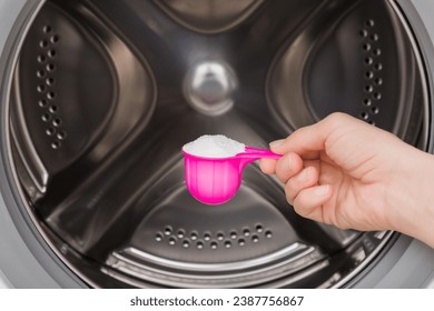 Young adult woman hand holding pink cup or scoop of white powder for clothes washing or washer descaling. Closeup. Front view.