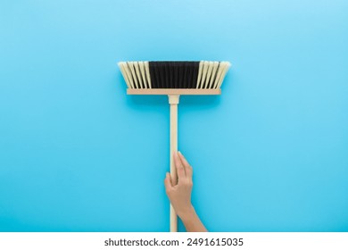 Young adult woman hand holding and showing new white black broom with wooden stick on light blue background. Pastel color. Closeup. Cleaning tool. Front view. - Powered by Shutterstock