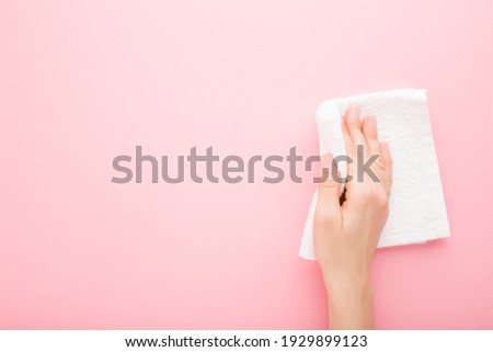 Young adult woman hand holding white rag and wiping table, wall or floor surface in kitchen, bathroom or other room. Closeup. Empty place for text or logo. Light pink background. Pastel color.