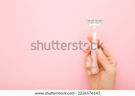 Young adult woman hand holding razor on light pink table background. Pastel color. Closeup. Female product for smooth body skin. Empty place for text.