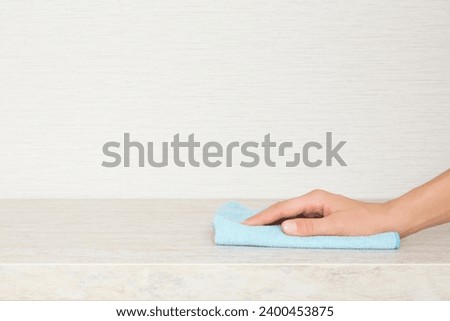 Young adult woman hand holding dry blue soft microfiber rag and wiping beige stone kitchen tabletop at home. Closeup. Cleaning service. Empty place for text on wallpaper background. Side view.