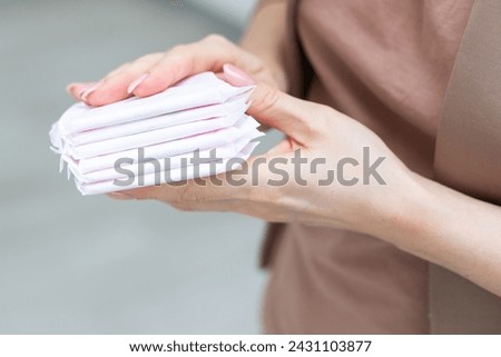 Young adult woman hand holding packs of sanitary towel on light p background. Pastel color. Closeup. Empty place for text.