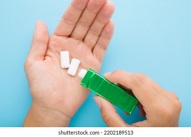 
Young adult woman hand pouring white chewing gum pads from green pack in opened palm on light blue table background. Pastel color. Closeup. Point of view shot.