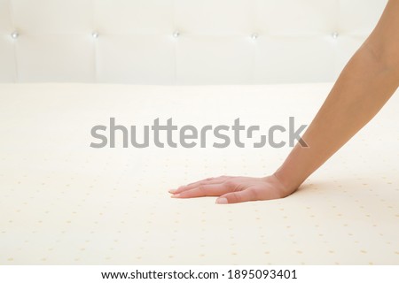 Young adult woman hand pressing yellow rubber foam mattress surface. Checking hardness and softness. Choice of the best type and quality. Closeup.