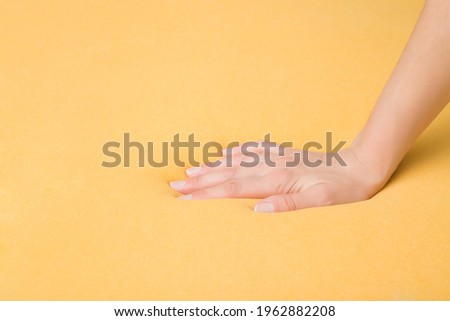 Young adult woman hand pressing yellow rubber foam mattress surface. Checking hardness and softness. Choice of the best type and quality. Closeup. Side view.