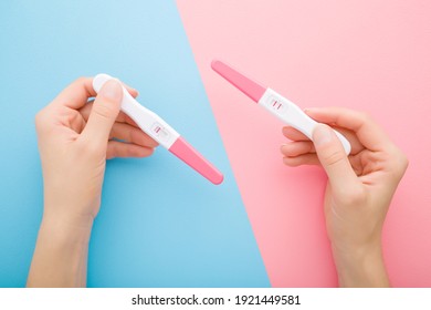 Young adult woman hands holding pregnancy tests with one stripe and two stripes on light blue pink table background. Pastel color. Negative and positive result. Closeup. Point of view shot. 