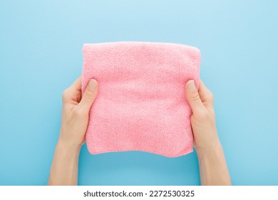Young adult woman hands holding pink folded dry soft microfiber rag for different surfaces wiping. Closeup. Light blue table background. Pastel color. Point of view shot.