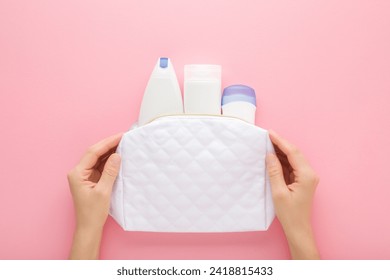 Young adult woman hands holding white cosmetic travel bag with plastic bottles on pink table background. Pastel color. Care about clean and body skin. Beauty products. Closeup. Point of view shot.