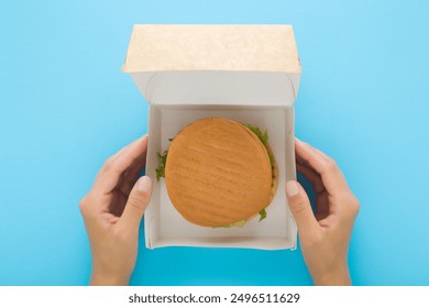 Young adult woman hands holding opened carton box with fresh burger on light blue table background. Pastel color. Closeup. Fast food delivery. Point of view shot. - Powered by Shutterstock