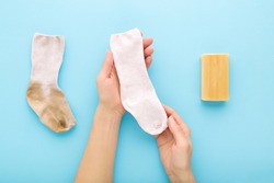 Young Adult Woman Hands Showing  Clean Child Sock After Washing With Household Soap On Light Blue Table Background. Pastel Color. Compare Dirty And Clean Socks. Closeup. Point Of View Shot.