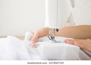 Young adult woman hands working with sewing machine and sewing white day curtains. Closeup. Side view. - Powered by Shutterstock