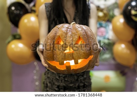 Young adult woman hold in hand spooky custom weird handmade orange pumpkin head with carved faces and glowing candle or light inside. Halloween party decoration celebrate traditional autumn holiday