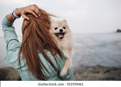 Young Adult  Woman Is Holding A Dog On Her Shoulder. Woman Turned Back 