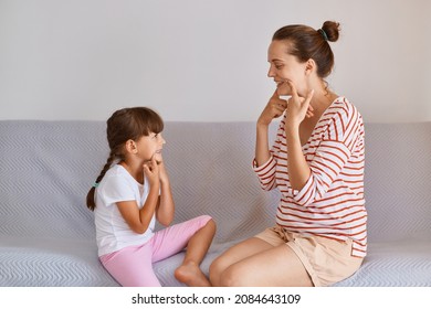 Young Adult Woman With Little Cute Girl Sitting Indoor On Gray Sofa And Having Language Lesson, Practicing Articulation, Speech Pathologist Demonstrates How To Pronounce Sounds.