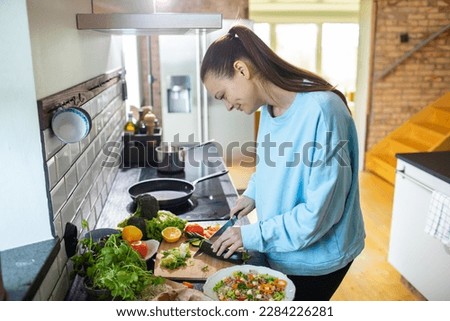 Young adult woman preparing a healthy salad in the kitchen