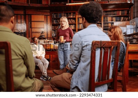 A young adult woman is standing and talking in a group mental health session with her peers.