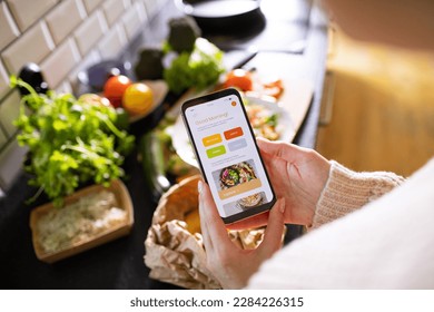 Young adult woman using a diet app on her phone while preparing a salad