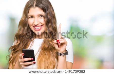 Young adult woman using smartphone surprised with an idea or question pointing finger with happy face, number one