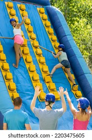 Young And Adult Women Using Sticks To Climb Up On Slide In Adventure Park.