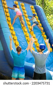 Young And Adult Women Using Sticks To Climb Up On Slide In Adventure Park.