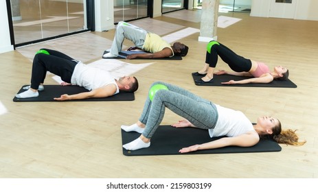 Young adults maintaining active lifestyle exercising with small pilates balls during group class in modern fitness center