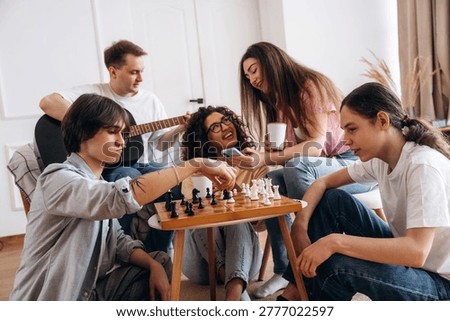 Young adults playing chess on a wooden table, with one person strumming a guitar in a cozy indoor space, showcasing casual interactions and leisure
