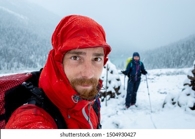 Young Adventure Healthy Couple Is Hiking Fryatt Valley Trail In Jasper National Park,  Alberta, Canada. Summer Snow Storm. Ginger Man In Red Rain Jacket Is Smiling To The Camera