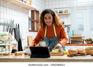 Mujer joven norteamericana africana aprendiendo en clases de cocina en línea a través de una computadora tablet en la cocina en casa