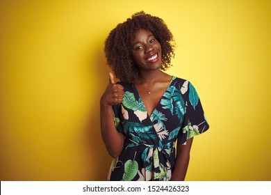 Young African Afro Woman Wearing Summer Floral Dress Over Isolated Yellow Background Doing Happy Thumbs Up Gesture With Hand. Approving Expression Looking At The Camera With Showing Success.